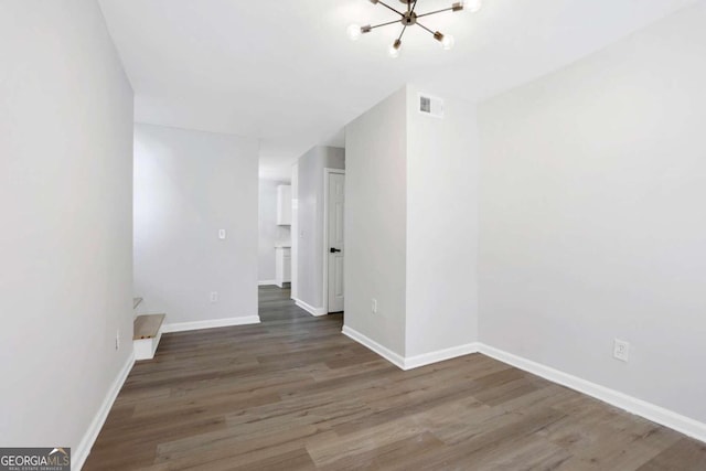 empty room with dark hardwood / wood-style flooring and a chandelier