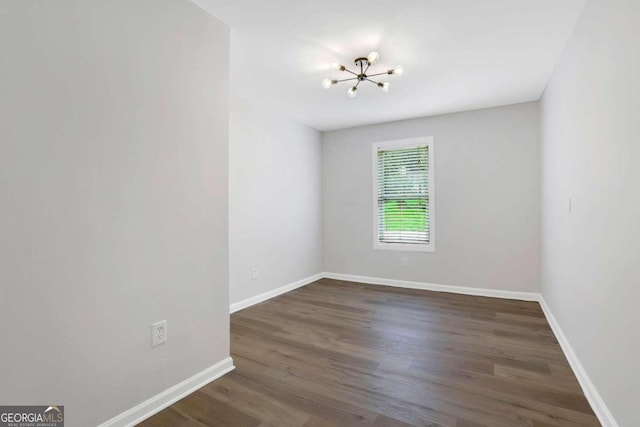 empty room featuring dark wood-type flooring and an inviting chandelier