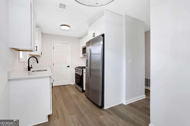 kitchen with stainless steel appliances, light hardwood / wood-style floors, white cabinets, and sink