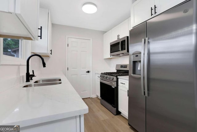 kitchen featuring light stone countertops, white cabinetry, stainless steel appliances, sink, and light hardwood / wood-style flooring