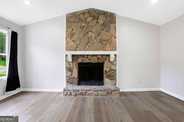 unfurnished living room with lofted ceiling, a stone fireplace, and hardwood / wood-style floors