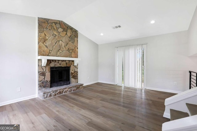 unfurnished living room with wood-type flooring, lofted ceiling, and a stone fireplace