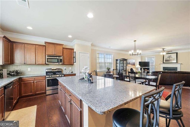 kitchen with appliances with stainless steel finishes, a kitchen island, decorative light fixtures, backsplash, and light stone counters