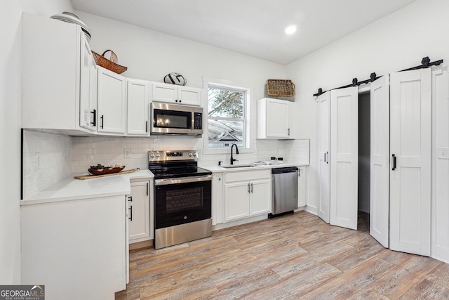 kitchen with a barn door, stainless steel appliances, tasteful backsplash, white cabinets, and sink