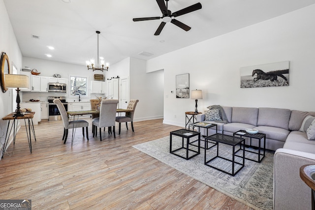 living room with ceiling fan with notable chandelier, sink, and light hardwood / wood-style flooring