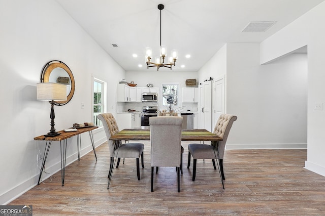 dining space featuring a chandelier, light hardwood / wood-style flooring, and a barn door