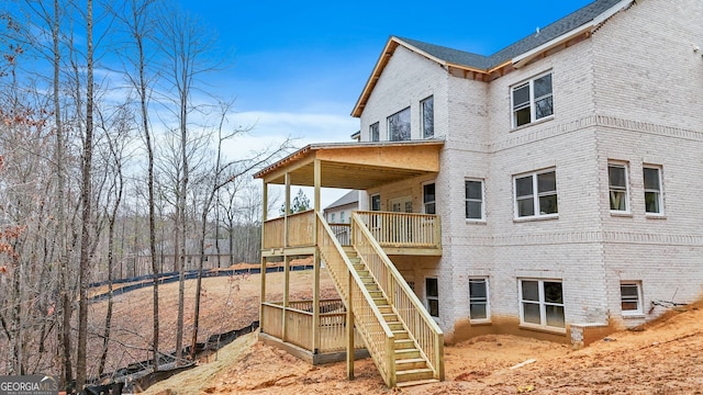 back of property featuring stairs, brick siding, and a deck