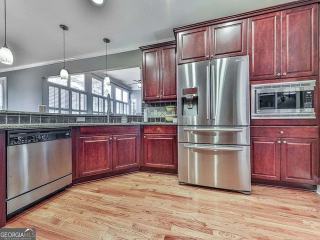 kitchen featuring stainless steel appliances, light wood-style flooring, a sink, ornamental molding, and hanging light fixtures