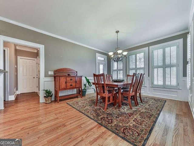 dining space with wainscoting, an inviting chandelier, light wood-style floors, crown molding, and a decorative wall