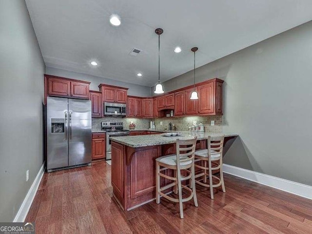 kitchen with pendant lighting, kitchen peninsula, sink, dark wood-type flooring, and appliances with stainless steel finishes