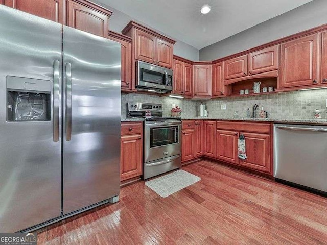 kitchen featuring hardwood / wood-style floors, stainless steel appliances, decorative backsplash, sink, and light stone counters