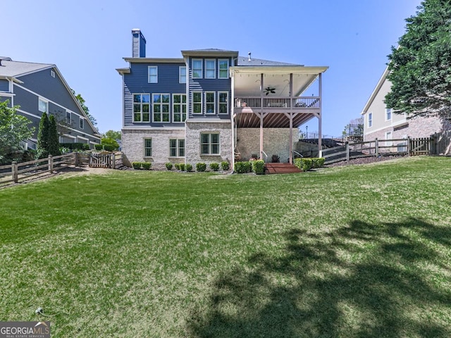 back of house featuring a chimney, a lawn, stone siding, a ceiling fan, and a fenced backyard