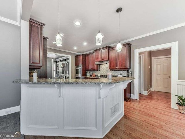 kitchen with decorative light fixtures, light hardwood / wood-style floors, a breakfast bar, decorative backsplash, and light stone counters