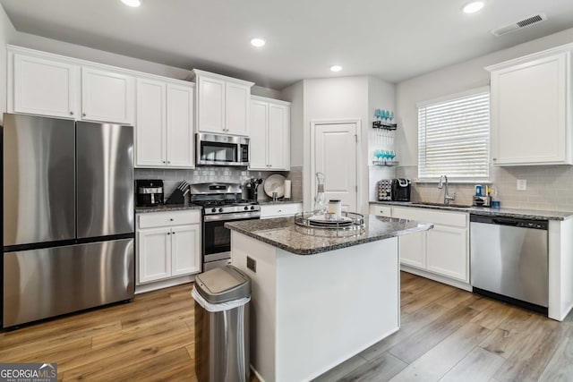 kitchen with sink, light wood-type flooring, a kitchen island, stainless steel appliances, and white cabinets