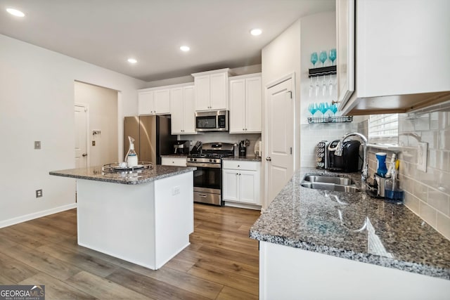 kitchen featuring sink, white cabinetry, dark stone countertops, stainless steel appliances, and a center island