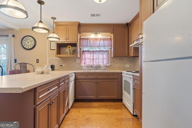 kitchen with kitchen peninsula, white appliances, light wood-type flooring, hanging light fixtures, and sink