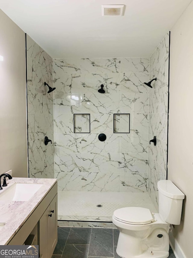 bathroom with toilet, a tile shower, and vanity