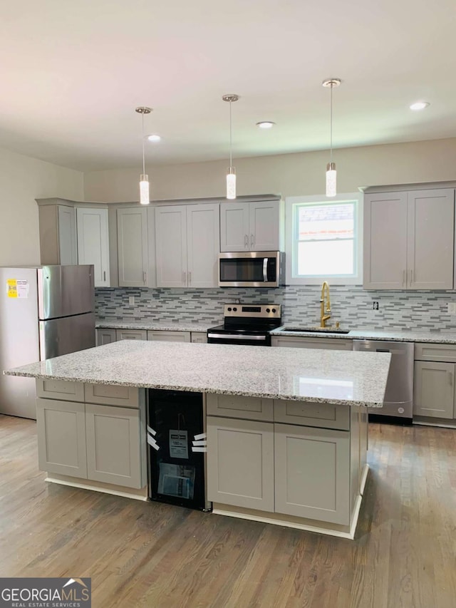 kitchen with stainless steel appliances, gray cabinetry, a center island, decorative light fixtures, and sink