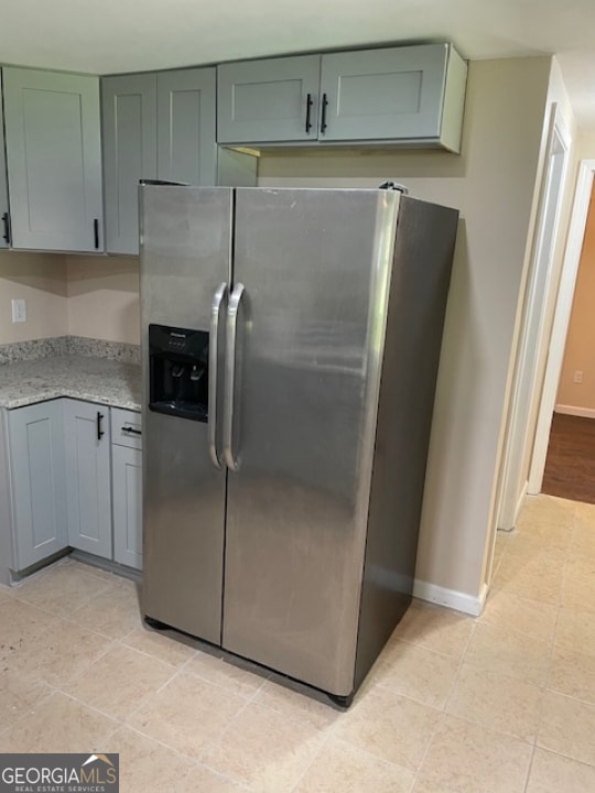 kitchen with stainless steel refrigerator with ice dispenser, light stone countertops, and light tile patterned flooring