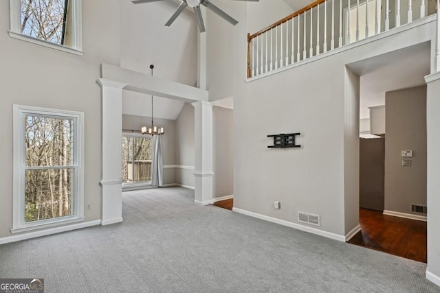 unfurnished living room with visible vents, a towering ceiling, baseboards, carpet flooring, and ceiling fan with notable chandelier