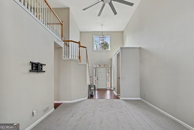 foyer entrance featuring dark carpet, baseboards, ceiling fan with notable chandelier, and a high ceiling