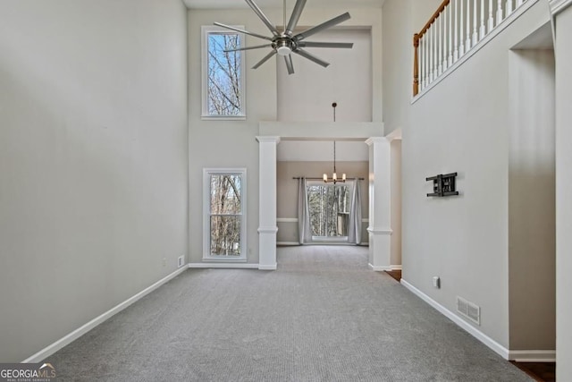 unfurnished living room with a high ceiling, decorative columns, plenty of natural light, and visible vents