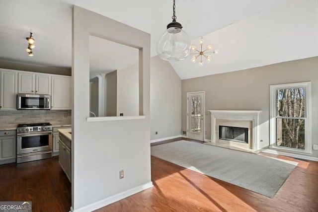 kitchen with appliances with stainless steel finishes, tasteful backsplash, vaulted ceiling, light countertops, and dark wood-type flooring