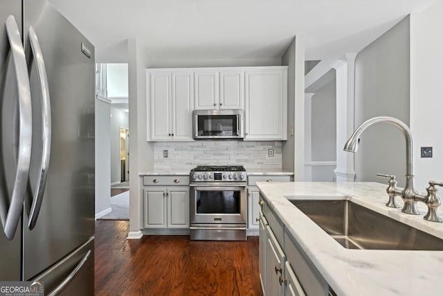 kitchen with decorative backsplash, dark wood-style flooring, light stone countertops, a sink, and stainless steel appliances
