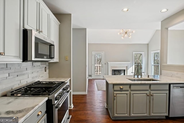 kitchen featuring appliances with stainless steel finishes, a sink, open floor plan, backsplash, and gray cabinetry