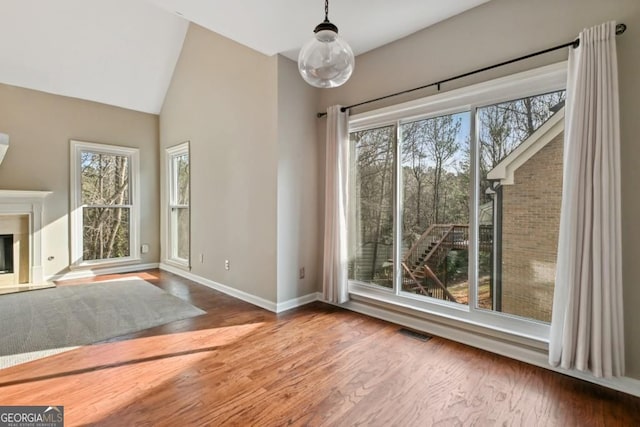 interior space featuring visible vents, wood finished floors, high vaulted ceiling, baseboards, and a glass covered fireplace