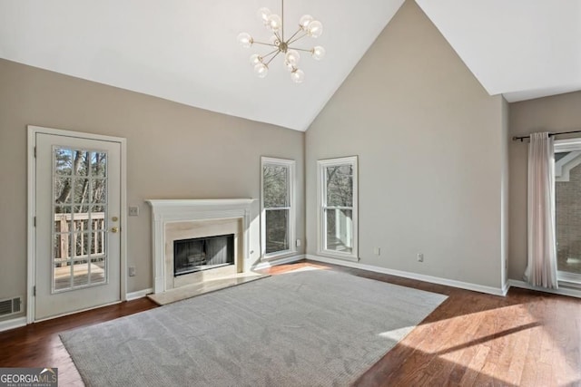 unfurnished living room featuring wood finished floors, a fireplace, baseboards, high vaulted ceiling, and a notable chandelier