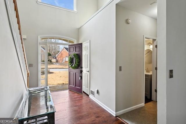 entrance foyer featuring baseboards, visible vents, wood finished floors, and a towering ceiling