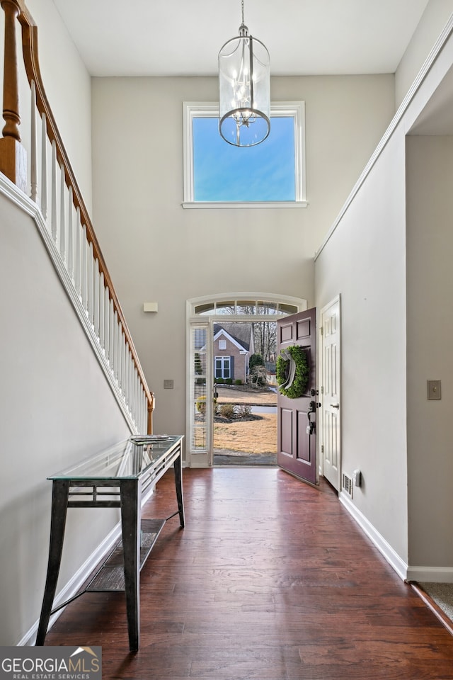 foyer entrance featuring dark wood-type flooring, a towering ceiling, and an inviting chandelier