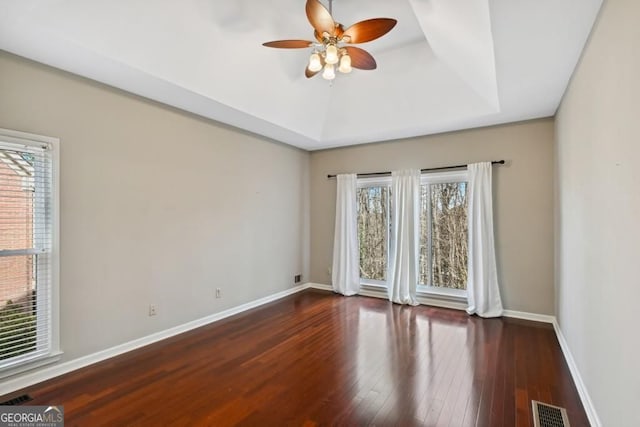 empty room with visible vents, wood-type flooring, baseboards, ceiling fan, and a tray ceiling