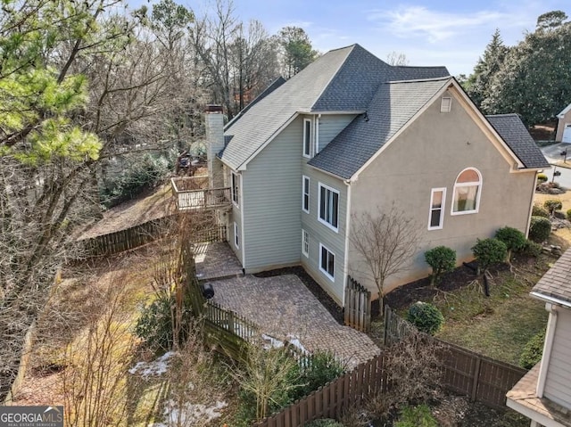 view of property exterior featuring fence private yard, a shingled roof, a patio area, and a chimney