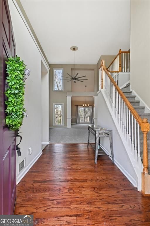 foyer entrance with ceiling fan with notable chandelier, baseboards, wood finished floors, visible vents, and stairway