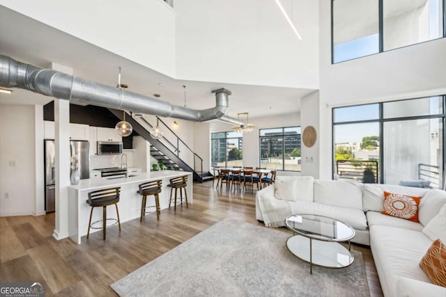 living room featuring sink, light hardwood / wood-style floors, a towering ceiling, and a notable chandelier