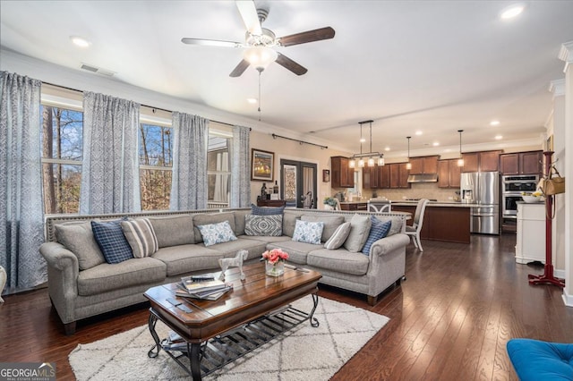 living room with dark wood-type flooring, ceiling fan with notable chandelier, and ornamental molding