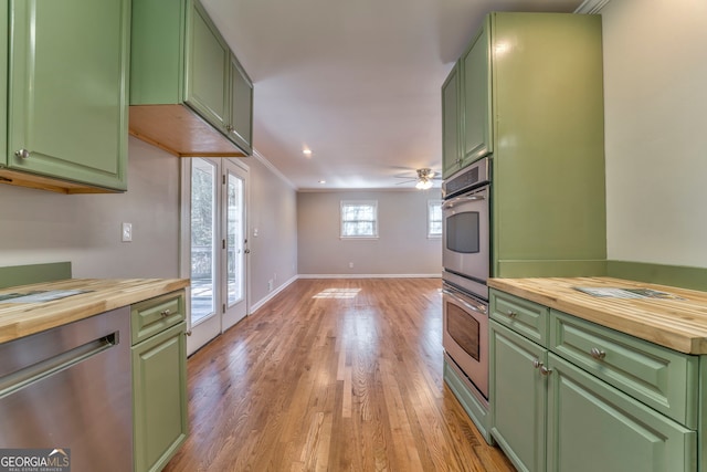 kitchen with green cabinets, butcher block counters, ornamental molding, light wood-type flooring, and stainless steel dishwasher