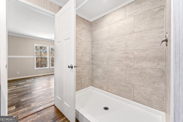 bathroom with wood-type flooring, crown molding, and tiled shower