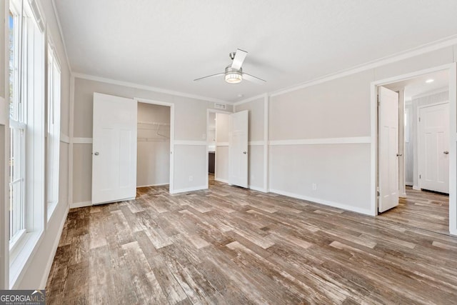 unfurnished bedroom with a spacious closet, ceiling fan, light wood-type flooring, a closet, and crown molding