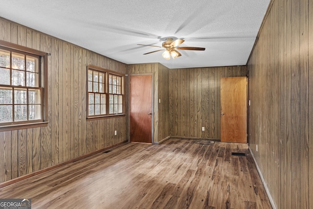 unfurnished room with ceiling fan, hardwood / wood-style floors, a textured ceiling, and wood walls