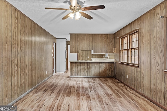 kitchen with wood walls, light wood-type flooring, ceiling fan, kitchen peninsula, and a textured ceiling