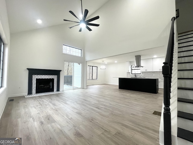 unfurnished living room with a high ceiling, ceiling fan, a fireplace, and light hardwood / wood-style floors