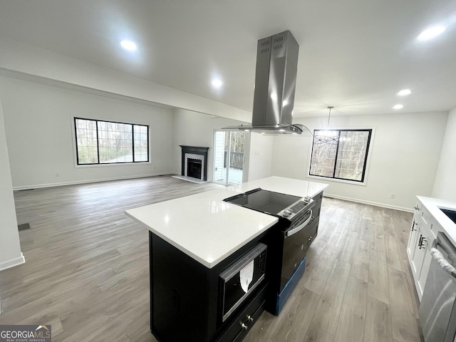 kitchen featuring white cabinetry, electric range, a kitchen island, island exhaust hood, and a brick fireplace