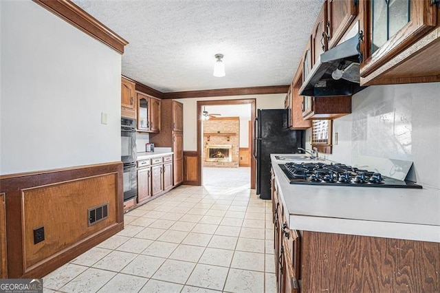 kitchen with ceiling fan, black double oven, a fireplace, a textured ceiling, and ornamental molding