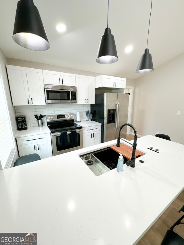 kitchen with white cabinets, stainless steel appliances, decorative backsplash, hanging light fixtures, and a breakfast bar area