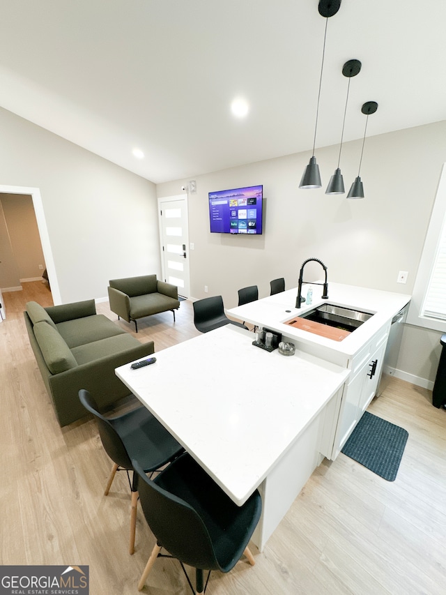 kitchen featuring white cabinets, decorative light fixtures, sink, a breakfast bar, and light hardwood / wood-style flooring