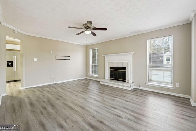 unfurnished living room featuring light wood-type flooring, ceiling fan, ornamental molding, and a tile fireplace