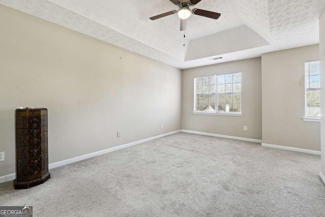 unfurnished room featuring a raised ceiling, ceiling fan, carpet, and a textured ceiling